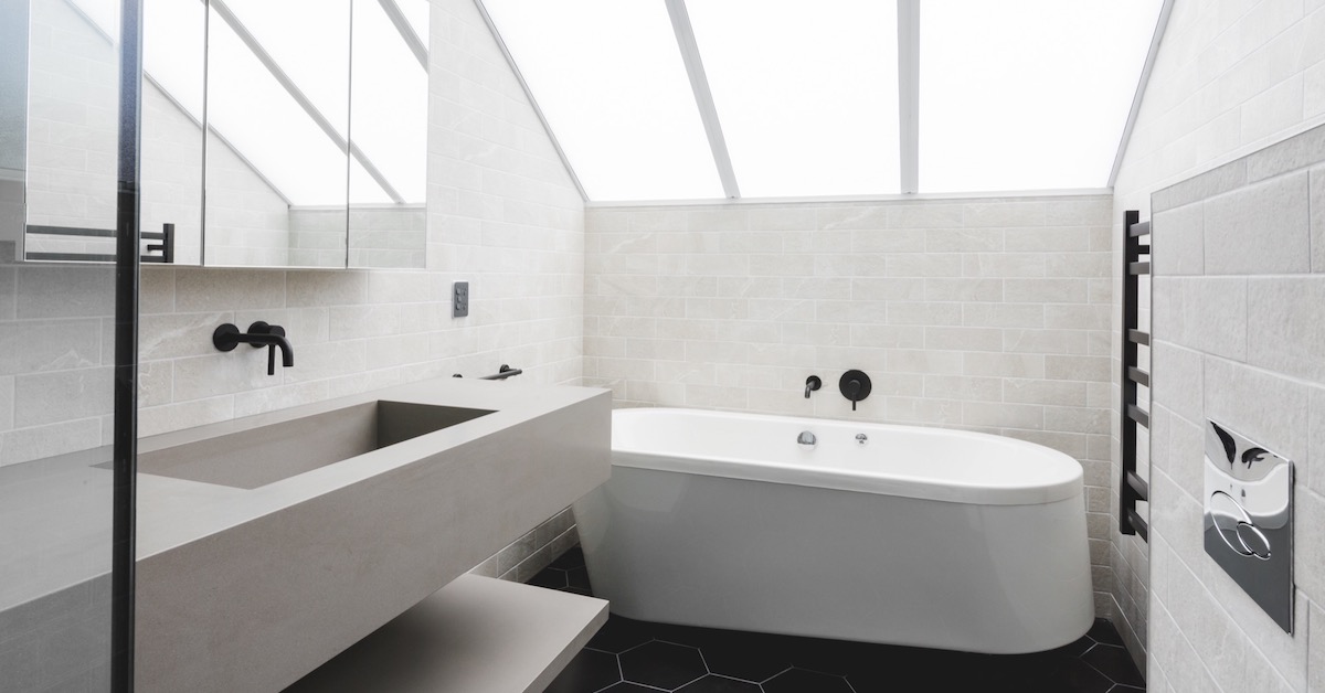 A modern white fully tiled finished bathroom remodel with a large skylight and stone benchtop. 